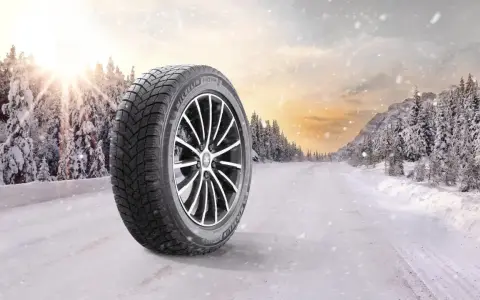 Michelin X-Ice Snow-däck på en snötäckt väg i en vinterskog. Solen bryter igenom molnen.