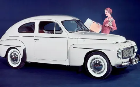 En elegant vit Volvo PV 444 med en kvinna och en hund bredvid.