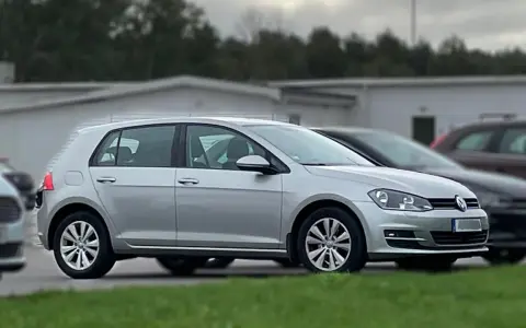 Silver Golf sportsvan parkerad på gräs. En mörkare bil syns bakom.