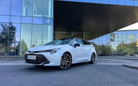 Vit Toyota Corolla Touring Sports framför en modern glasbyggnad. Inga problem med denna bil, bara ren stil.