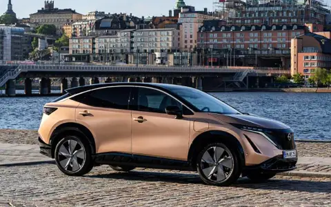Nissan Ariya testkörning i Stockholm. En elegant elbil parkerad vid vattnet med stadens silhuett i bakgrunden.