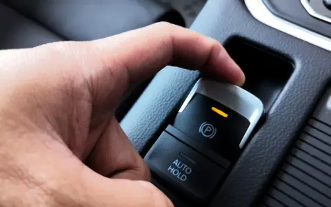 En hand trycker på knappen för elektronisk handbroms som låst sig. En orange lampa lyser.