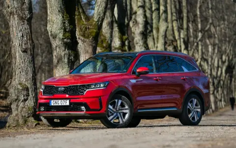 Röd Kia Sorento parkerad längs en trädkantad grusväg. En person syns i bakgrunden, kanske på väg att undersöka ett eventuellt kia sorento problem.