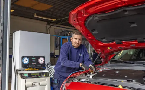 Mekaniker arbetar med bilens AC-system. Lär dig hur fungerar ac i bilen med denna serviceutrustning.