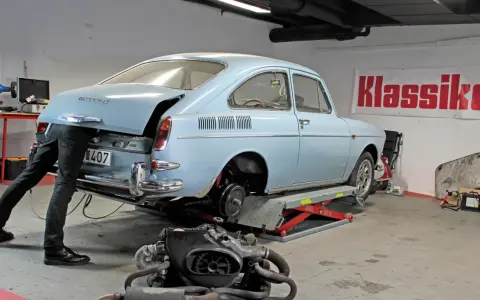 Mekaniker arbetar med en ljusblå vw typ 3 i verkstad. Motorn ligger framför bilen.