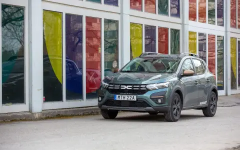 Grön Dacia Sandero Stepway, redo för ett däcktest. Bilen står parkerad framför en byggnad med färgglada fönster.