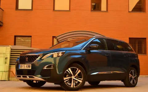 Mörkblå Peugeot 5008 SUV parkerad framför en orange tegelbyggnad. En perfekt bil för en familjeresa, en riktig peugeot 5008 test.