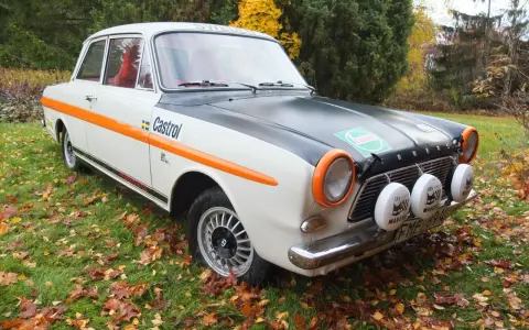 Ford Taunus 12M i rallystuk, med orange detaljer och Castrol-logga, står på en gräsmatta täckt av höstlöv.