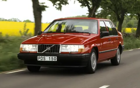 En röd 740 Volvo kör längs en landsväg, med en gul rapsåker och träd i bakgrunden.