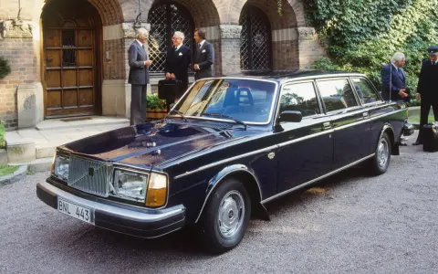 Mörkblå Volvo 264 Bertone limousine parkerad framför en byggnad med män i kostym.