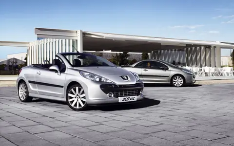 Två silverfärgade Peugeot 207 CC cabriolet står parkerade på en stenlagd uteplats framför en modern byggnad.