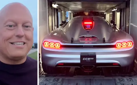En man ler bredvid en silverfärgad Koenigsegg CC850 som lastas in i en trailer.