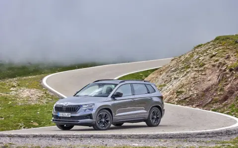 Grå Skoda Karoq på en slingrig bergsväg, omgiven av dimma och grönska. Inga problem här, bara en vacker utsikt.