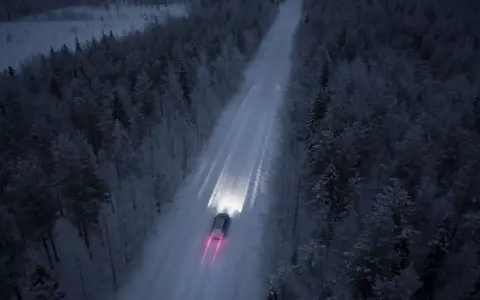 Bil kör på snöig skogsväg i mörker, halvljus symbolen lyser upp vägen.