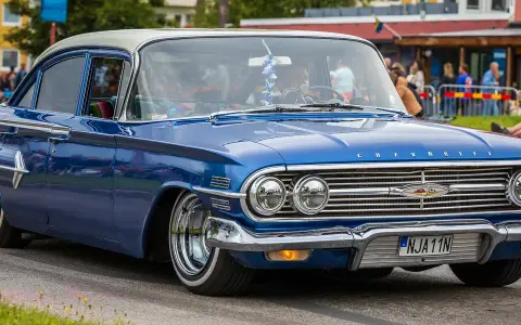 En blå klassisk bil, en Chevrolet, rullar fram på en gata.