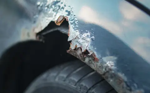 Detaljerad bild av rostskador på en bilskärm, en tydlig indikation på att det är dags att laga rost på bilen. Däcket syns nedtill.