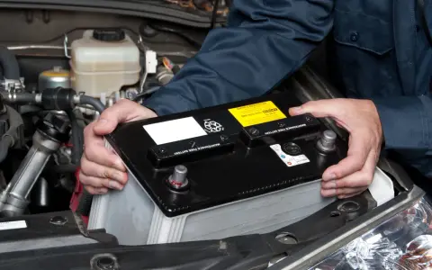 Mekaniker byter ett urladdat bilbatteri i motorutrymmet.