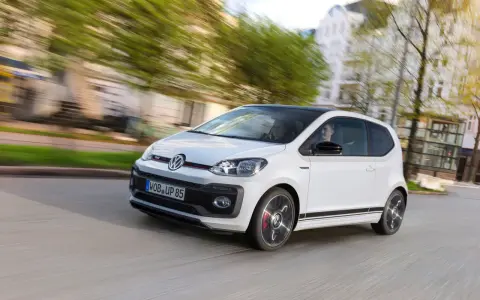 Vit VW Up GTI med svarta detaljer kör genom en stad.