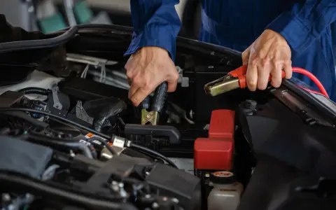 Mekaniker kopplar startkablar till bilbatteriet. Frågan "hur lång tid tar det att ladda ett bilbatteri" är relevant här.