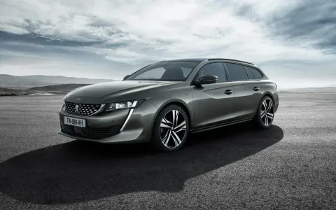 Grå Peugeot 508 SW står parkerad på en asfalterad yta med berg i bakgrunden. En perfekt bil för ett peugeot 508 test.