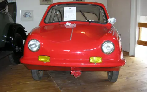 En röd, rundad bil, en Messerschmitt KR200, står på ett trägolv. Fram king Fulda.