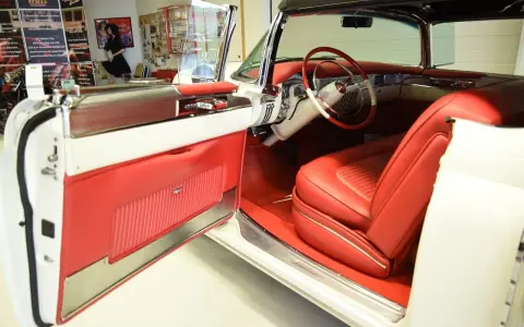 En vit cabriolet Cadillac från 50-talet med lyxig röd interiör. Dörren är öppen och visar upp säten och instrumentbräda.