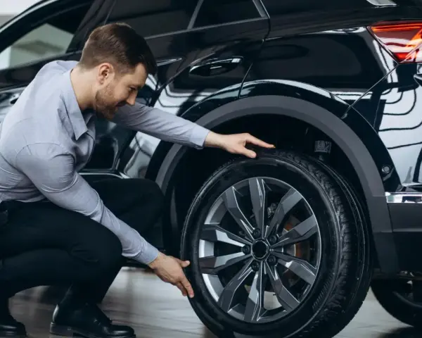 Man inspekterar däcket på en svart bil, redo för ett kumho ecsta ps71 test.