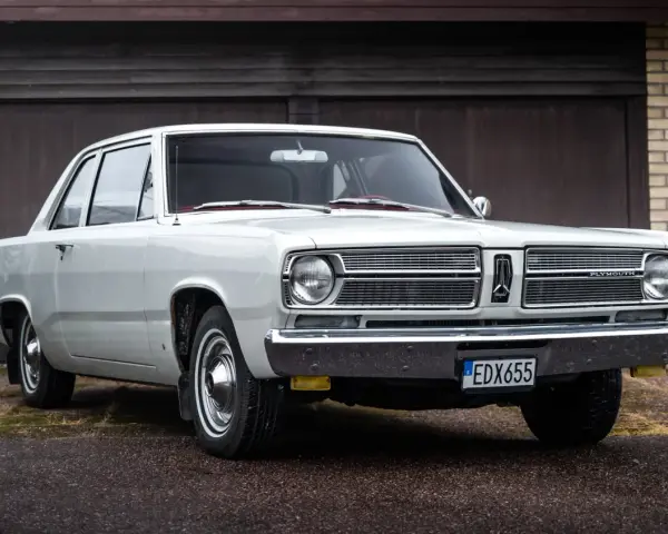 En vit, klassisk Plymouth Valiant står parkerad framför ett garage.