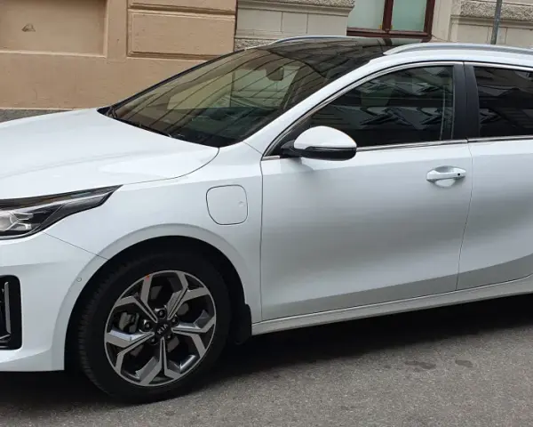Vit Kia Ceed SW Plug-in Hybrid parkerad på gata. En elsparkcykel syns i bakgrunden.