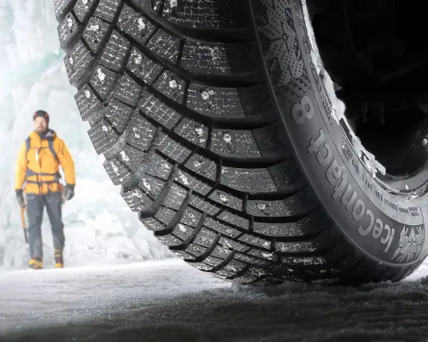En man i gul jacka står framför en isvägg. Ett Continental IceContact 3-däck med dubb är i förgrunden, redo för test.
