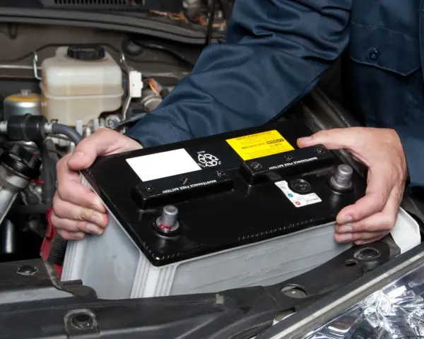 Personen håller i ett bilbatteri för att koppla in det i bilen.