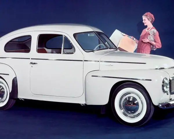 En elegant vit Volvo PV 444 med en kvinna och en hund bredvid.