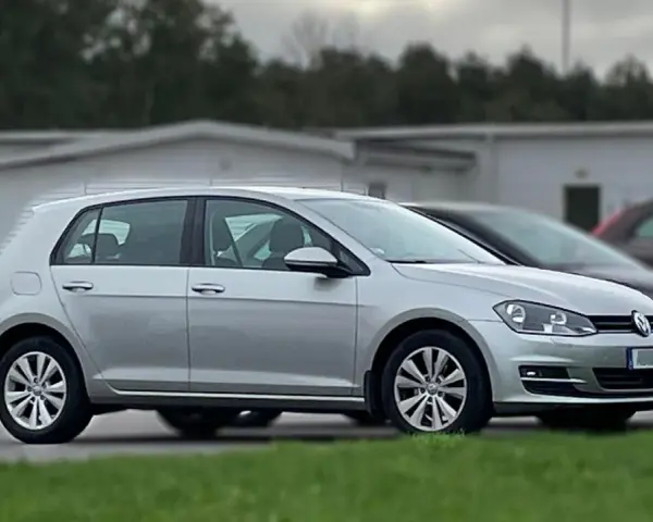Silver Golf sportsvan parkerad på gräs. En mörkare bil syns bakom.