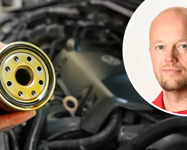 En hand håller ett oljefilter, redo att byta det för att stoppa vobblande ljud från bilen. En man i rött syns i bakgrunden.