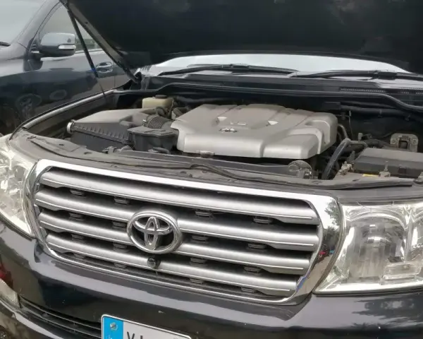 Motorhuven på en svart p0420 Toyota Land Cruiser är öppen, vilket visar V8-motorn. En annan likadan bil står bredvid.