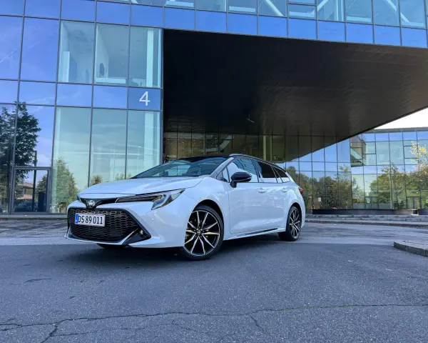 Vit Toyota Corolla Touring Sports framför en modern glasbyggnad. Inga problem med denna bil, bara ren stil.