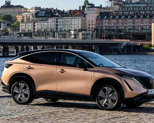 Nissan Ariya testkörning i Stockholm. En elegant elbil parkerad vid vattnet med stadens silhuett i bakgrunden.