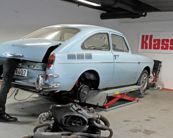 Mekaniker arbetar med en ljusblå vw typ 3 i verkstad. Motorn ligger framför bilen.