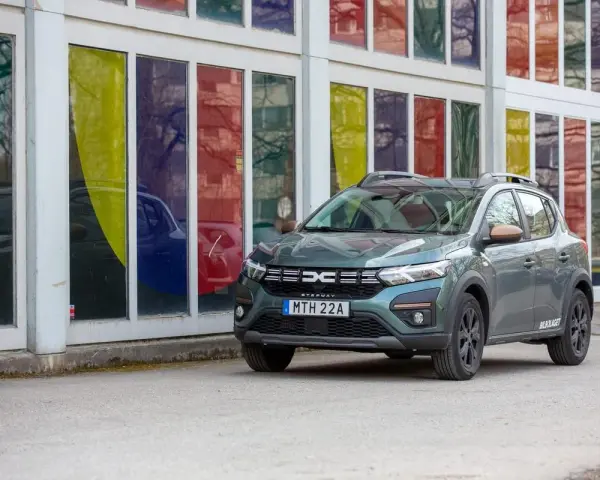 Grön Dacia Sandero Stepway, redo för ett däcktest. Bilen står parkerad framför en byggnad med färgglada fönster.