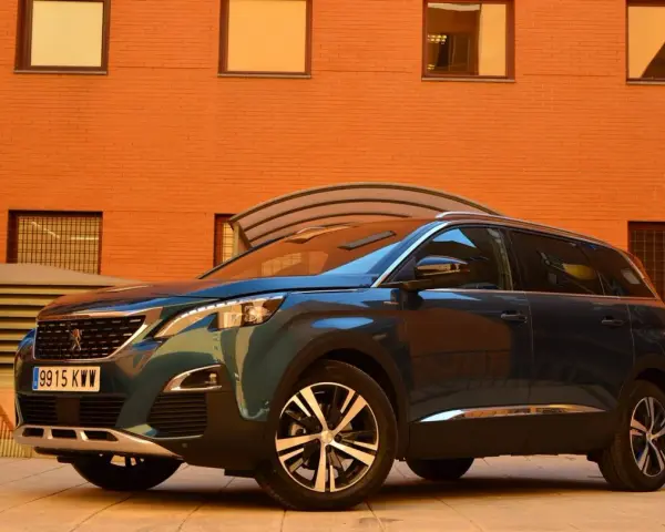 Mörkblå Peugeot 5008 SUV parkerad framför en orange tegelbyggnad. En perfekt bil för en familjeresa, en riktig peugeot 5008 test.