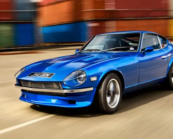 Blå Nissan Datsun 240Z kör förbi färgglada fraktcontainrar.
