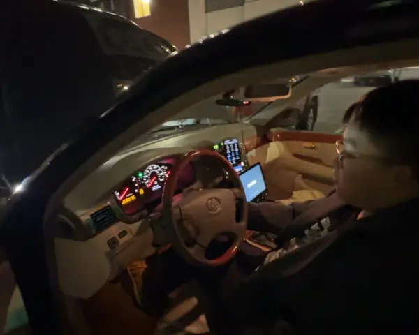 Personen försöker starta bilen, men den startar inte, bara klickar. Motorhuven är öppen och en laptop är på passagerarsätet.