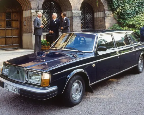 Mörkblå Volvo 264 Bertone limousine parkerad framför en byggnad med män i kostym.