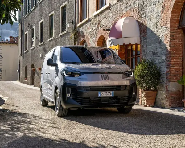En grå Fiat Doblo står parkerad på en smal gata i Italien. En vacker byggnad med tegel och sten syns i bakgrunden.