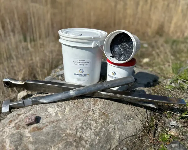 Fett till dragkrok och verktyg ligger på en sten. Två burkar med fett, varav en öppen, syns bredvid.