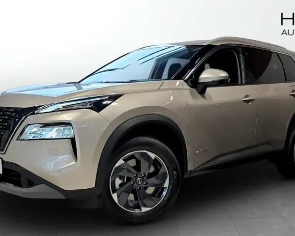 A tan Nissan X-Trail e-POWER SUV is shown from the front three-quarter view in a showroom.