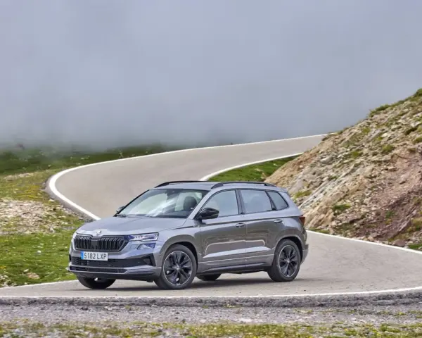 Grå Skoda Karoq på en slingrig bergsväg, omgiven av dimma och grönska. Inga problem här, bara en vacker utsikt.