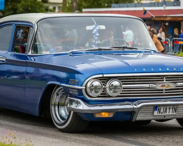 En blå klassisk bil, en Chevrolet, rullar fram på en gata.