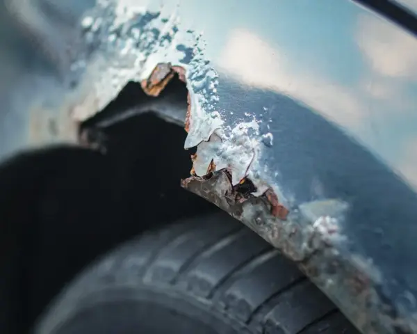 Detaljerad bild av rostskador på en bilskärm, en tydlig indikation på att det är dags att laga rost på bilen. Däcket syns nedtill.
