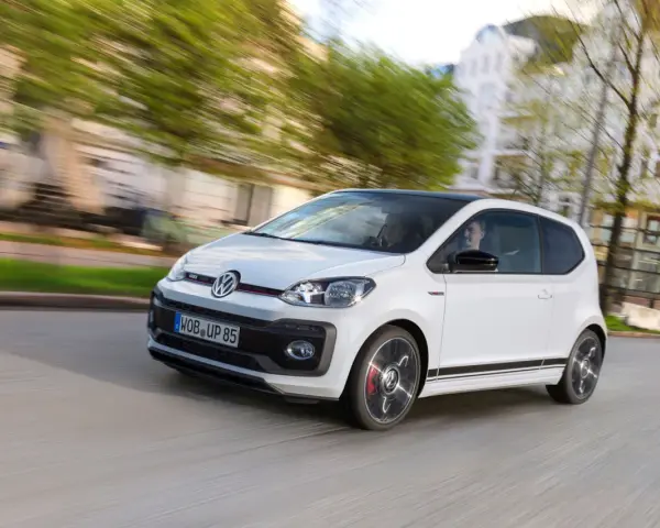 Vit VW Up GTI med svarta detaljer kör genom en stad.
